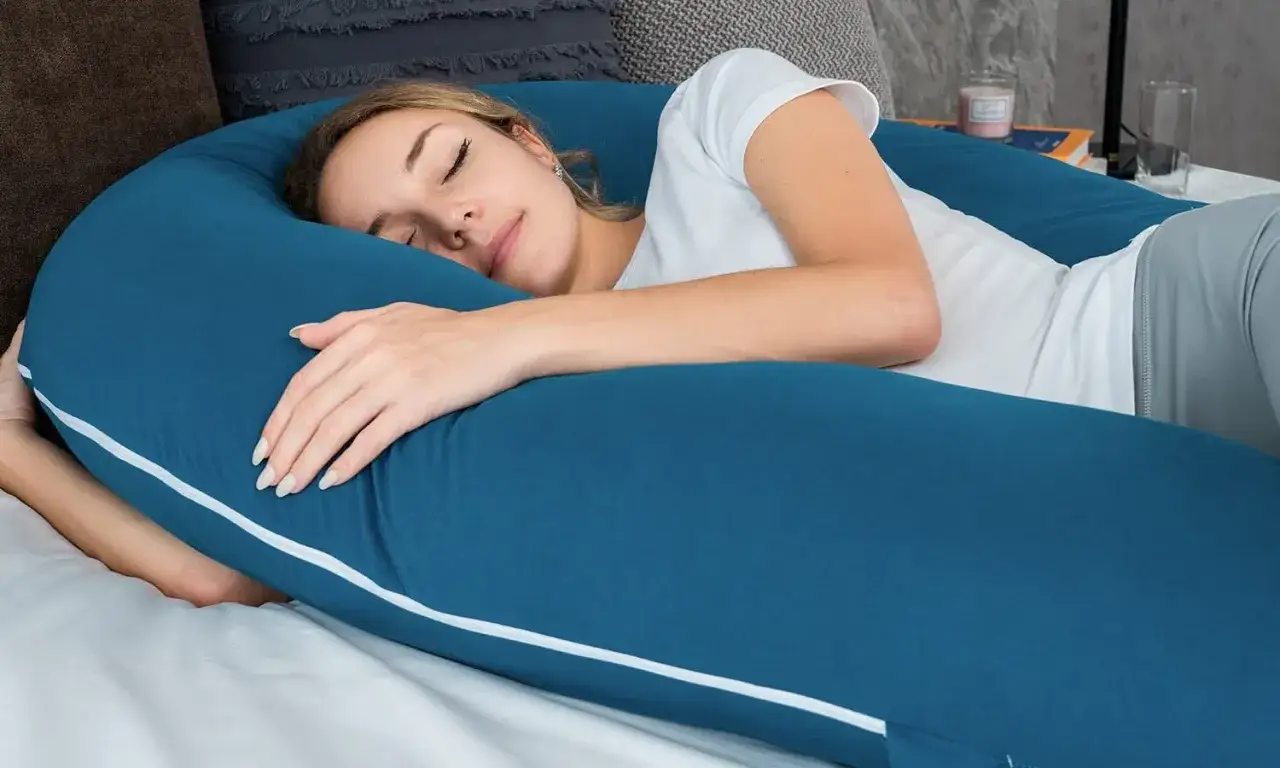 Donna dorme serenamente abbracciando un cuscino a forma di U, una soluzione ideale per chi cerca come dormire con il mal di schiena e trovare sollievo.