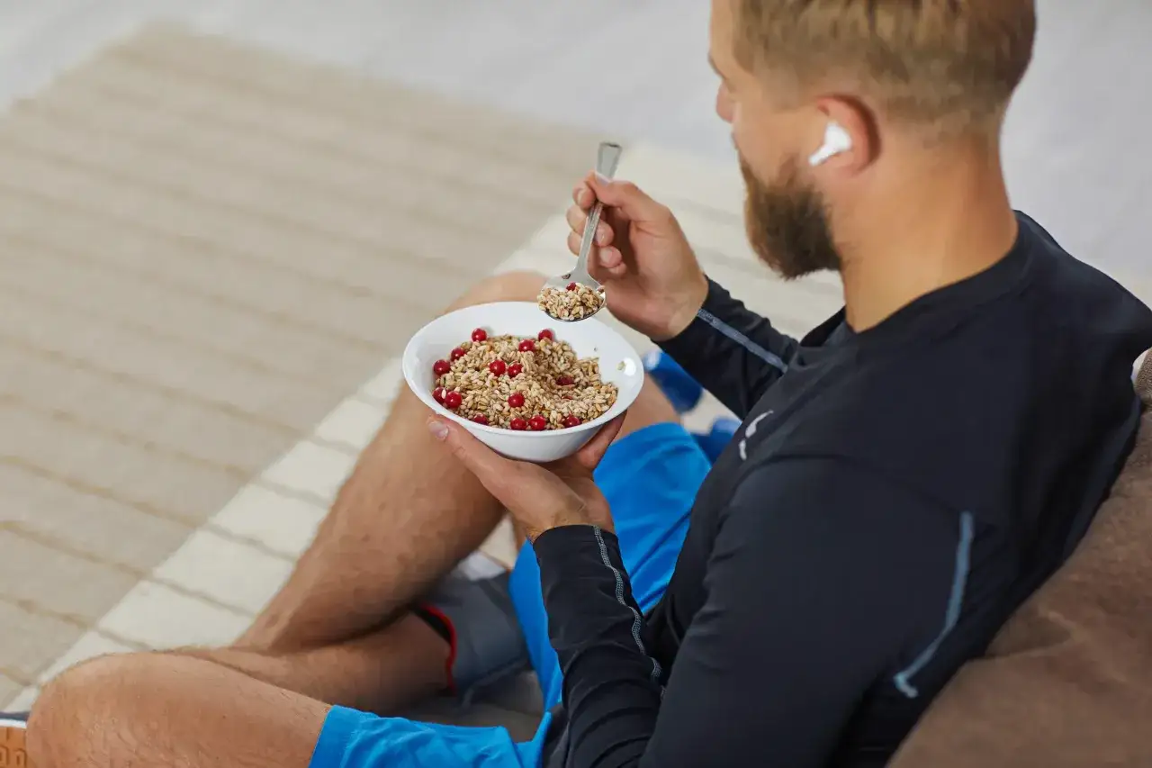 Uomo con barba mangia fiocchi d'avena e mirtilli rossi, ottimi carboidrati complessi quali sono per energia duratura.