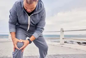 Uomo con tuta grigia si tiene il ginocchio, preoccupato per come sbloccare un ginocchio bloccato.