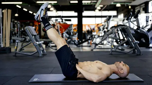 Uomo muscoloso esegue reverse crunch su panca in palestra, concentrato sull'allenamento addominale.