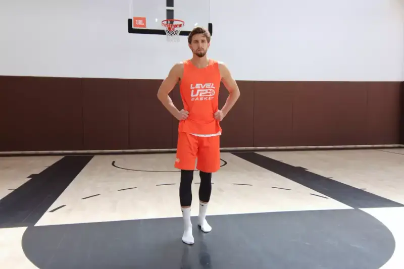 Giocatore di basket in tenuta arancione, mani sui fianchi, con enfasi sui muscoli del bacino laterali.